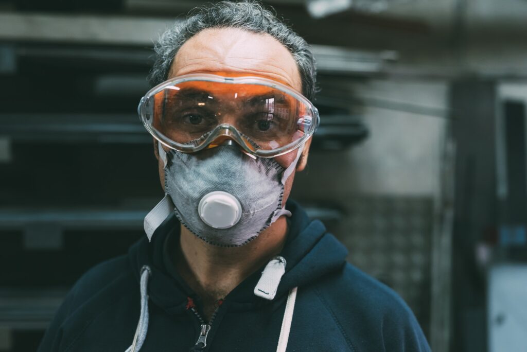 Portrait of metalworker in dust mask and safety goggles in forge workshop